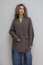 vrouw met donkerbruine oversized blazer en koffie in hand leunt tegen groene deur