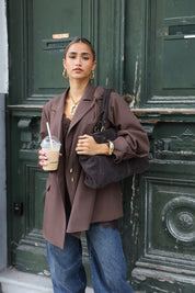 vrouw met donkerbruine oversized blazer en jeans kijkt recht vooruit bij groene deur