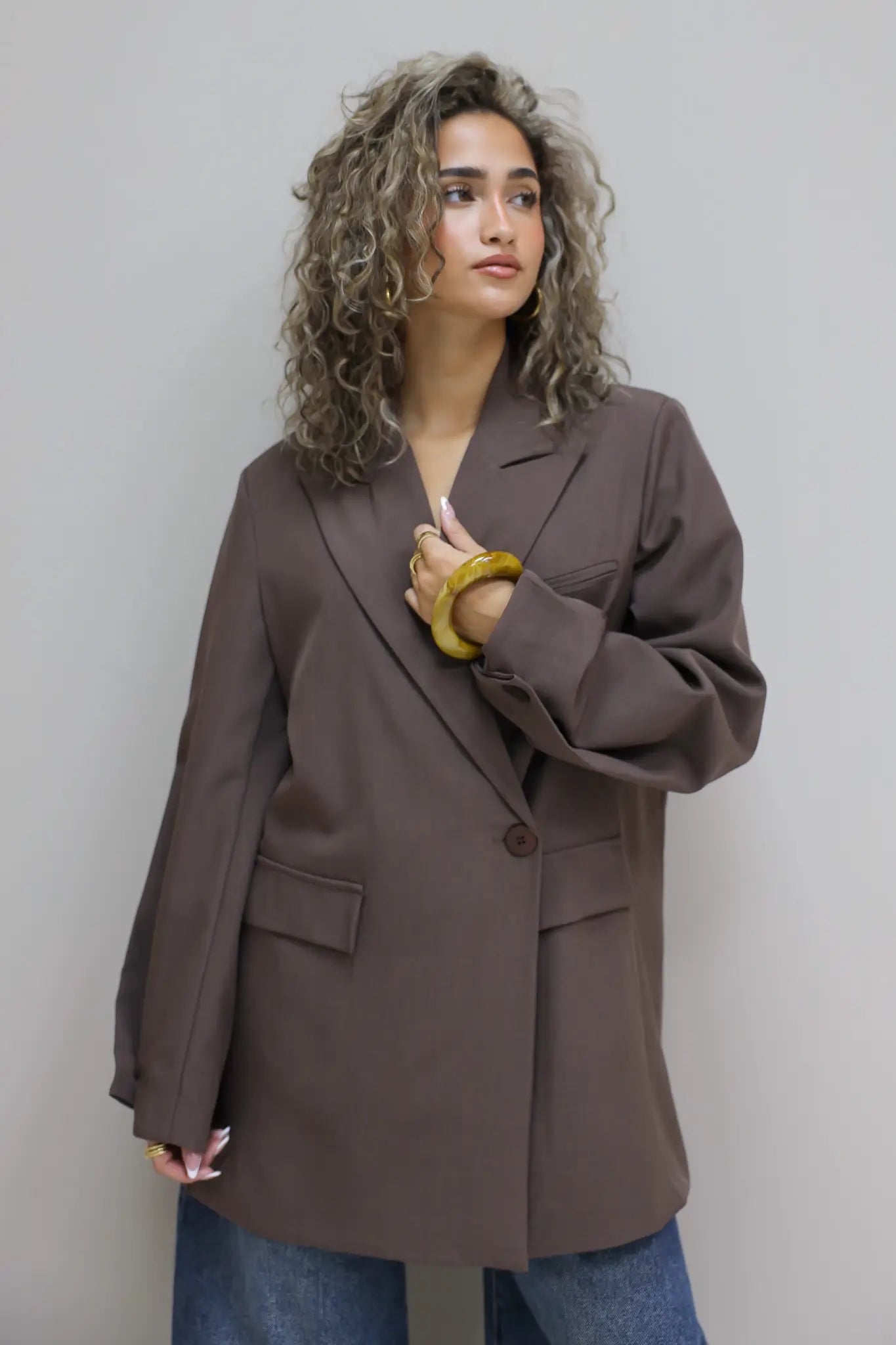 zijaanzicht van vrouw met donkerbruine oversized blazer die over haar schouder kijkt