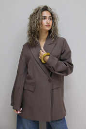 zijaanzicht van vrouw met donkerbruine oversized blazer die over haar schouder kijkt