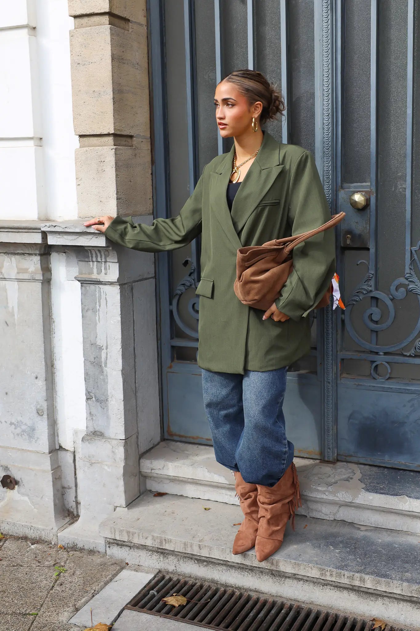 vrouw draagt groene oversized blazer met bruine tas over schouder voor blauwe deur