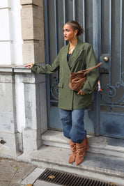 vrouw draagt groene oversized blazer met bruine tas over schouder voor blauwe deur