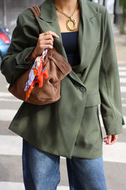 vrouw draagt groene oversized blazer met bruine tas en sjaaltje over schouder op straat