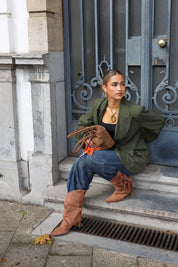 vrouw met groene oversized blazer en bruine laarzen zit op stoep bij blauwe deur