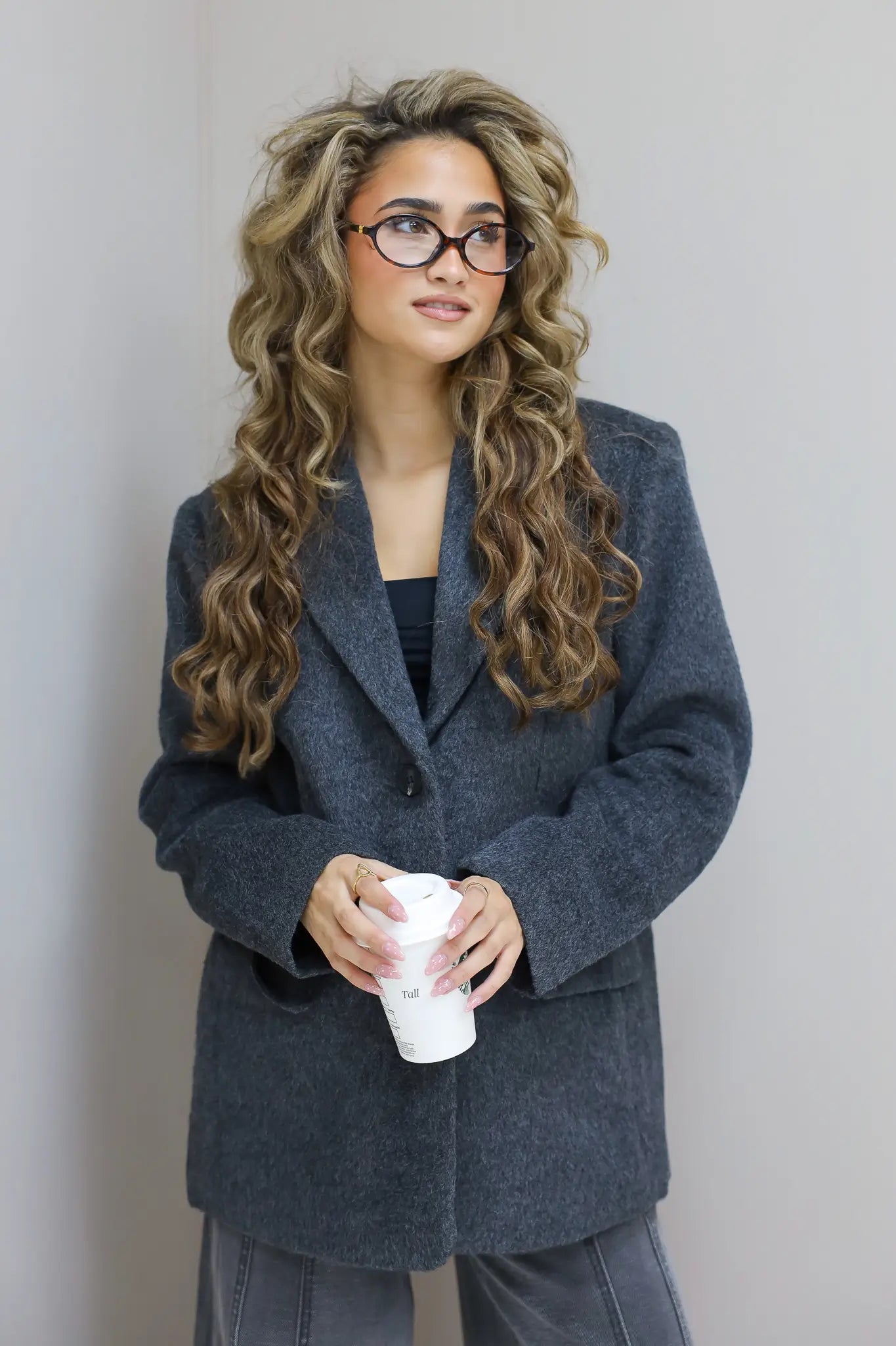 Model met donkergrijze wolblazer, kijkt recht vooruit, handen in zakken