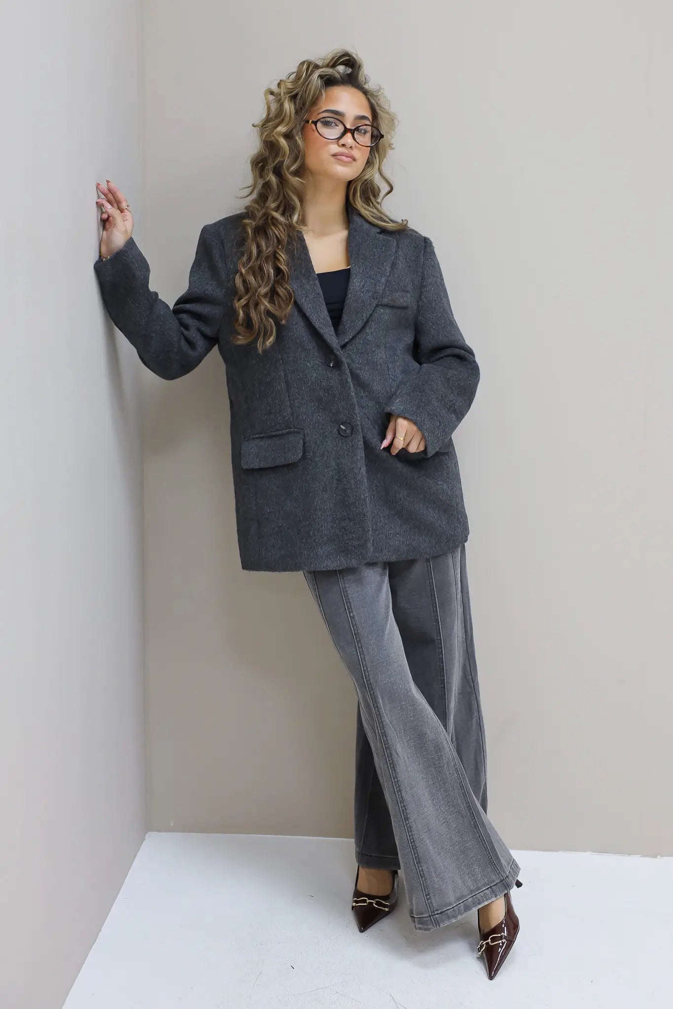 Model met blazer tegen lichte muur, ontspannen pose met één hand in zak