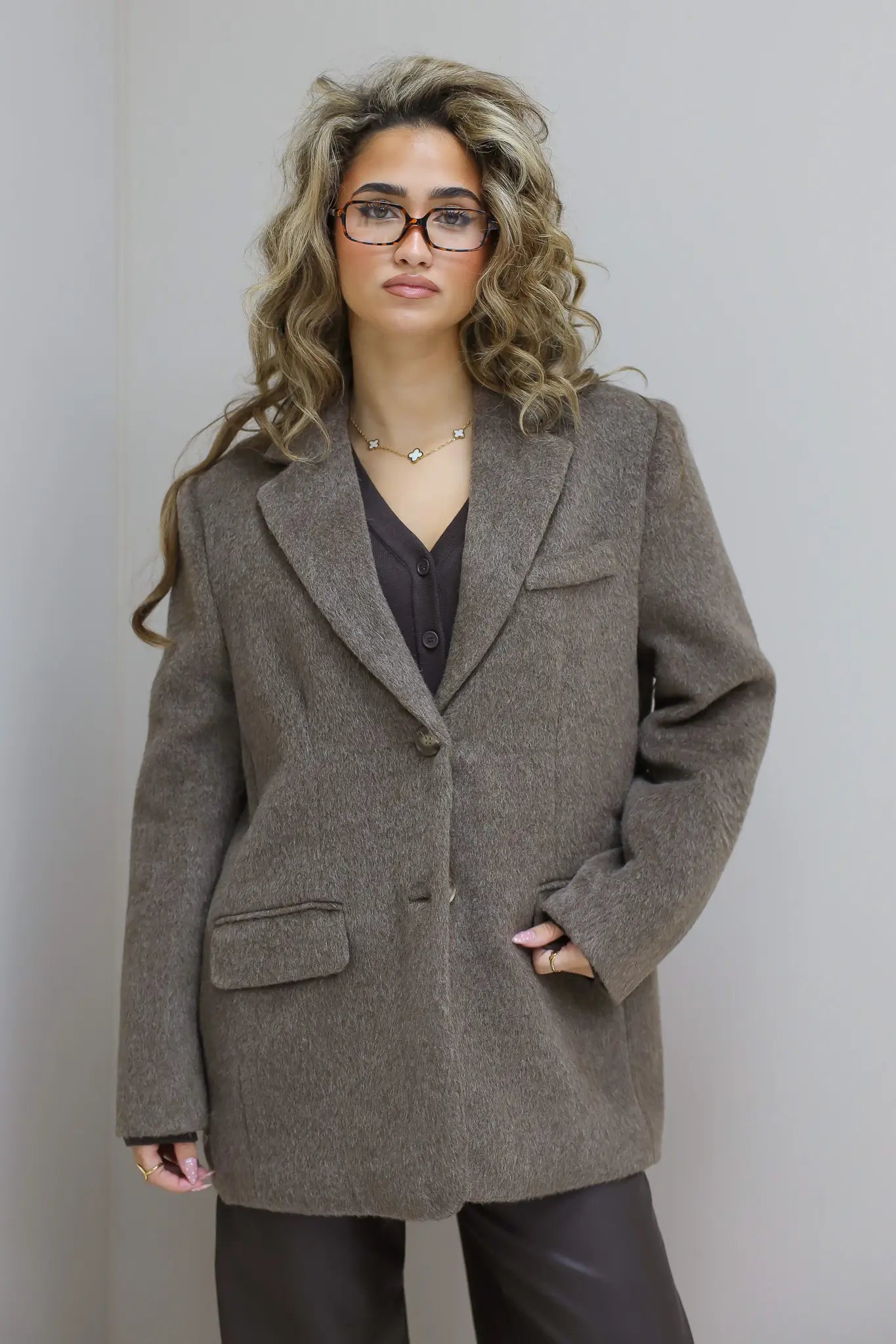 Model poseert tegen muur, taupe blazer los gedragen