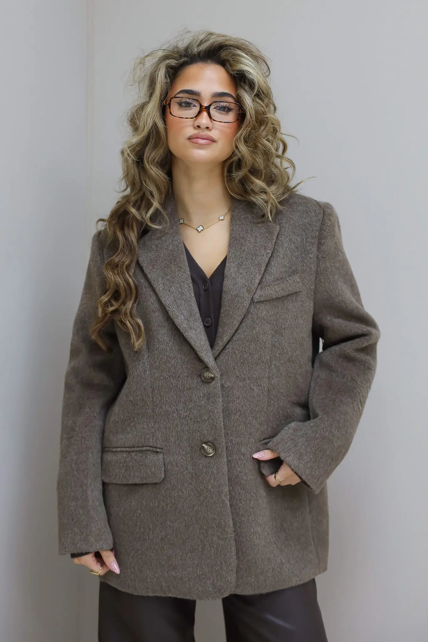 Model met taupe wollen blazer, bril en golvend haar, recht voor camera
