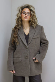 Model met taupe wollen blazer, bril en golvend haar, recht voor camera