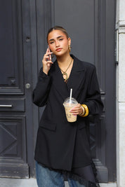 close up van vrouw met zwarte oversized blazer en strakke vlecht tegen stadsmuur