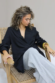 vrouw zit op stoel met hand in haar en draagt zwarte oversized blazer open