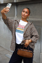 Camel blouse met ruitjes en capuchon open gedragen over een wit T-shirt met kleurrijke newspaper opdruk