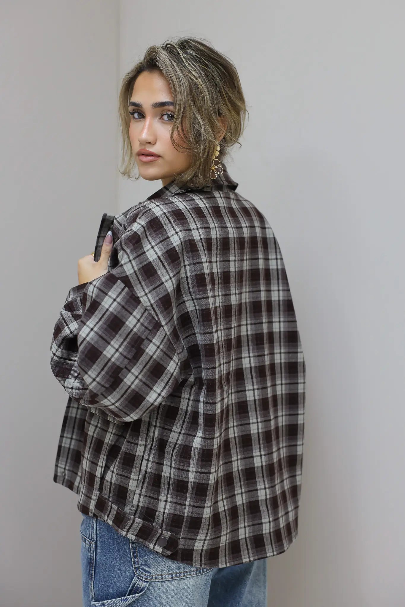 zijaanzicht van vrouw met bruine geruite blouse, kijkt over schouder tegen grijze muur