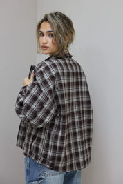 zijaanzicht van vrouw met bruine geruite blouse, kijkt over schouder tegen grijze muur