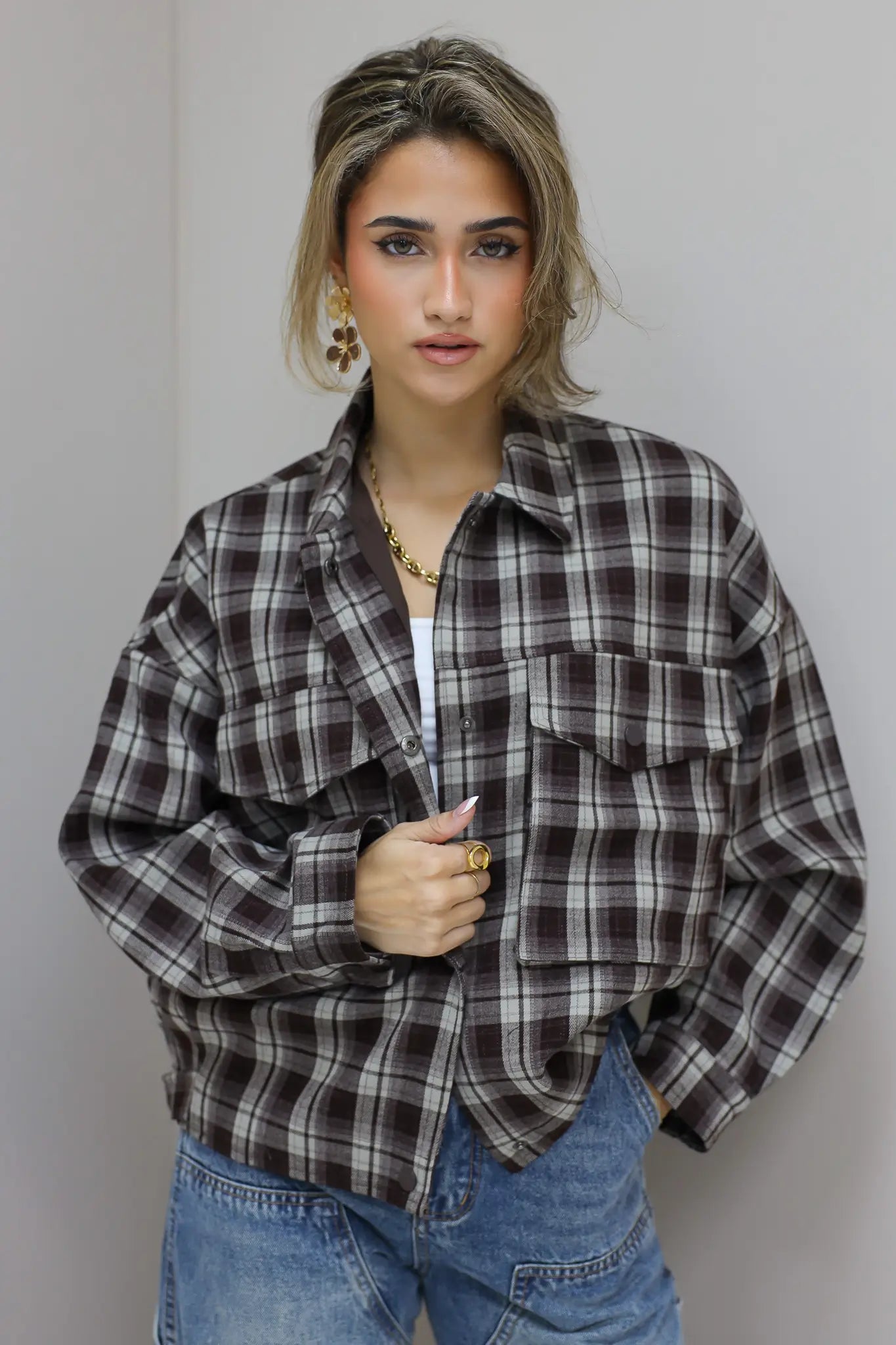 vrouw draagt bruine geruite blouse half open en kijkt omhoog tegen grijze muur