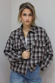 vrouw draagt bruine geruite blouse half open en kijkt omhoog tegen grijze muur