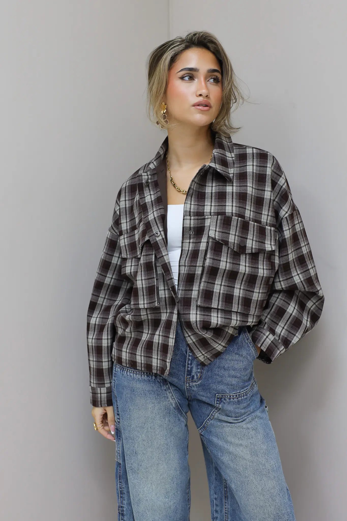 vrouw met bruine geruite blouse houdt kraag vast en kijkt opzij