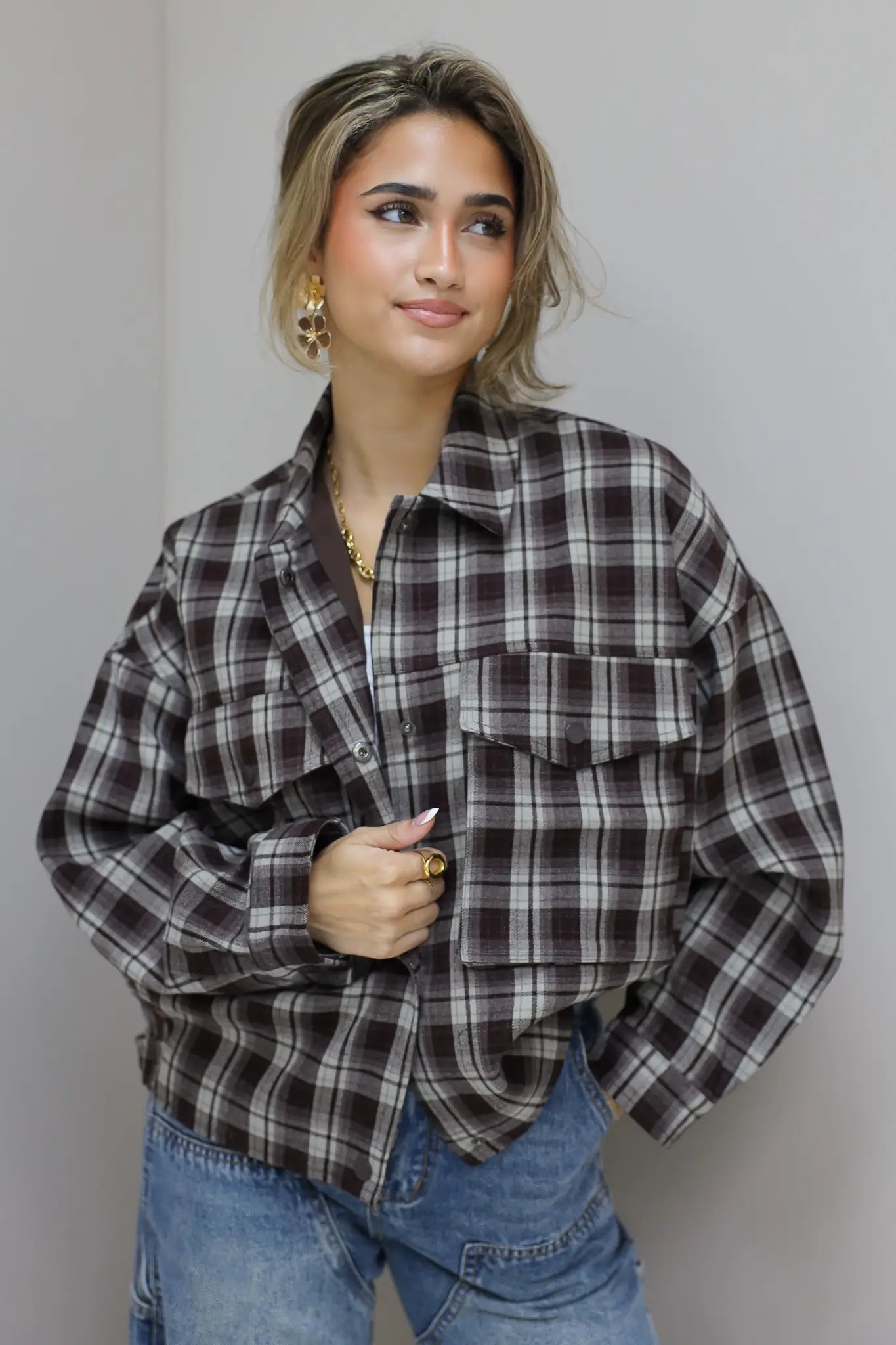 vrouw draagt bruine geruite blouse deels open met hand aan borst