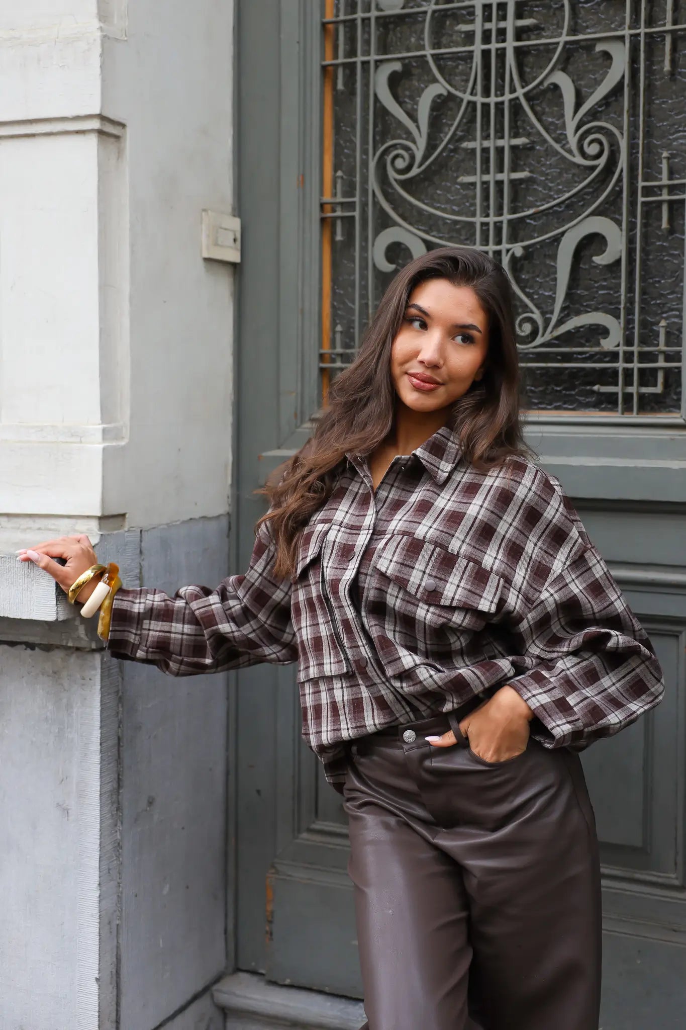 vrouw draagt bruine geruite blouse en kijkt recht in camera met hand aan haar
