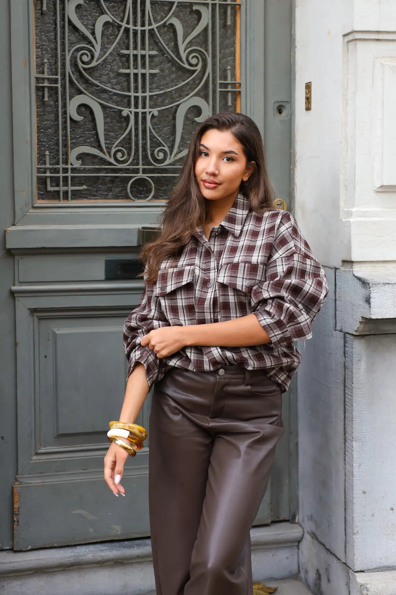 vrouw met bruine geruite blouse leunt tegen deur en houdt arm omhoog