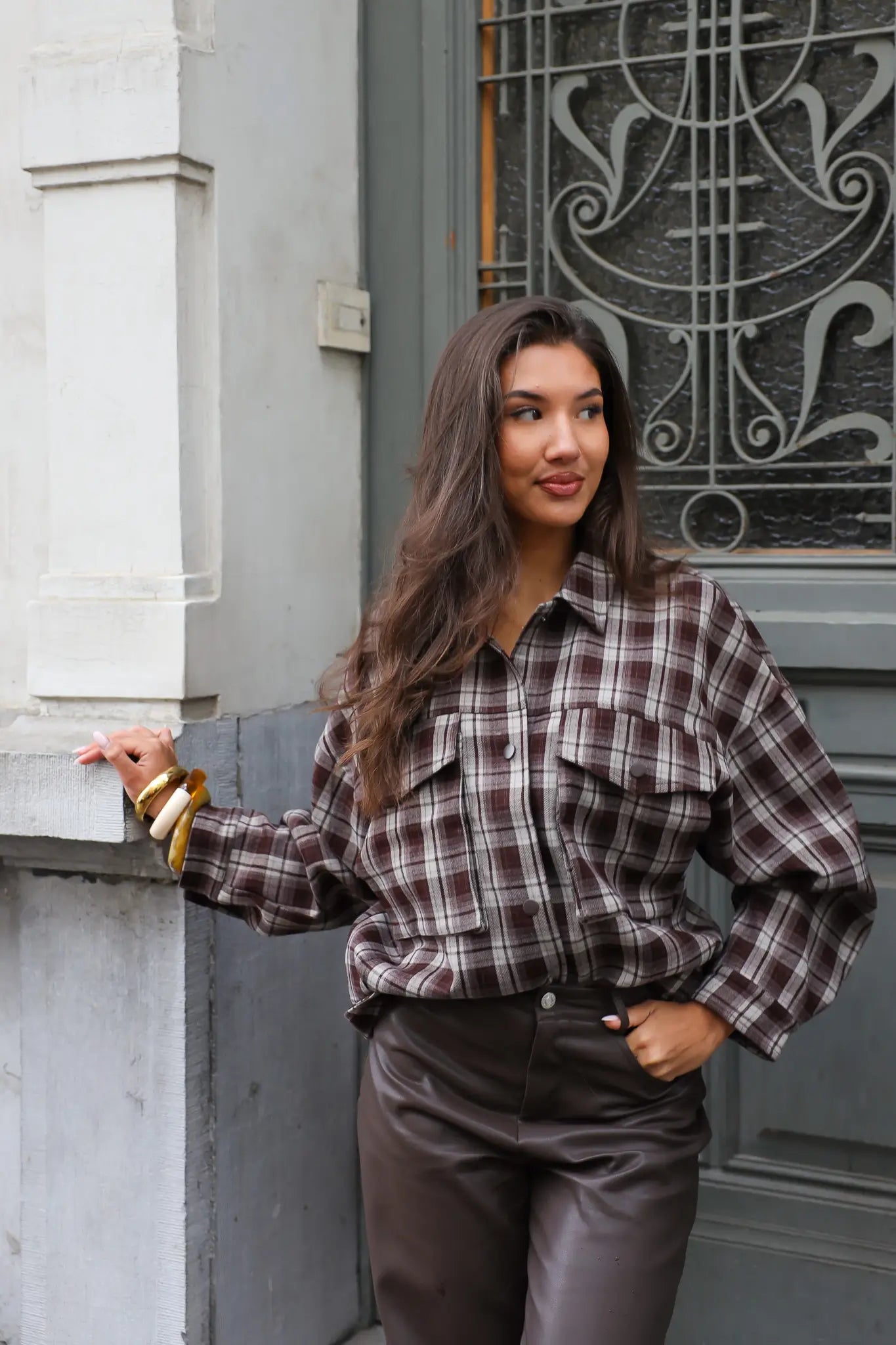 vrouw met bruine geruite blouse kijkt opzij en houdt hand aan muur