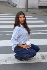 model hurkt met blauw wit gestreepte blouse en jeans op straat