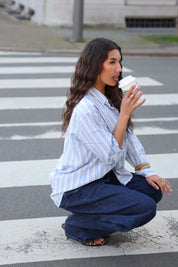 model zit op straat met blauw wit gestreepte blouse en jeans