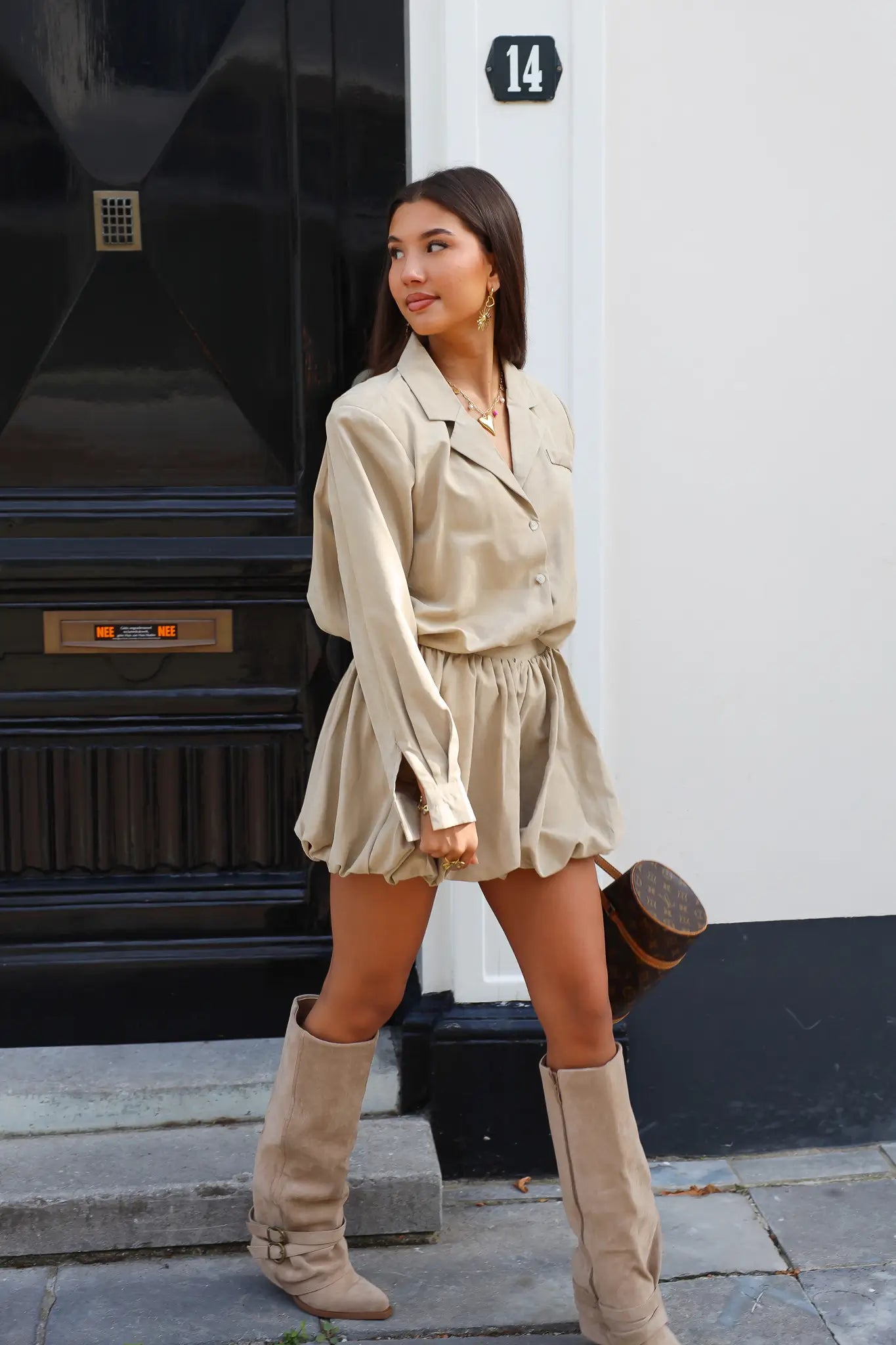 Model in beige blouse met rok en laarzen buiten op straat