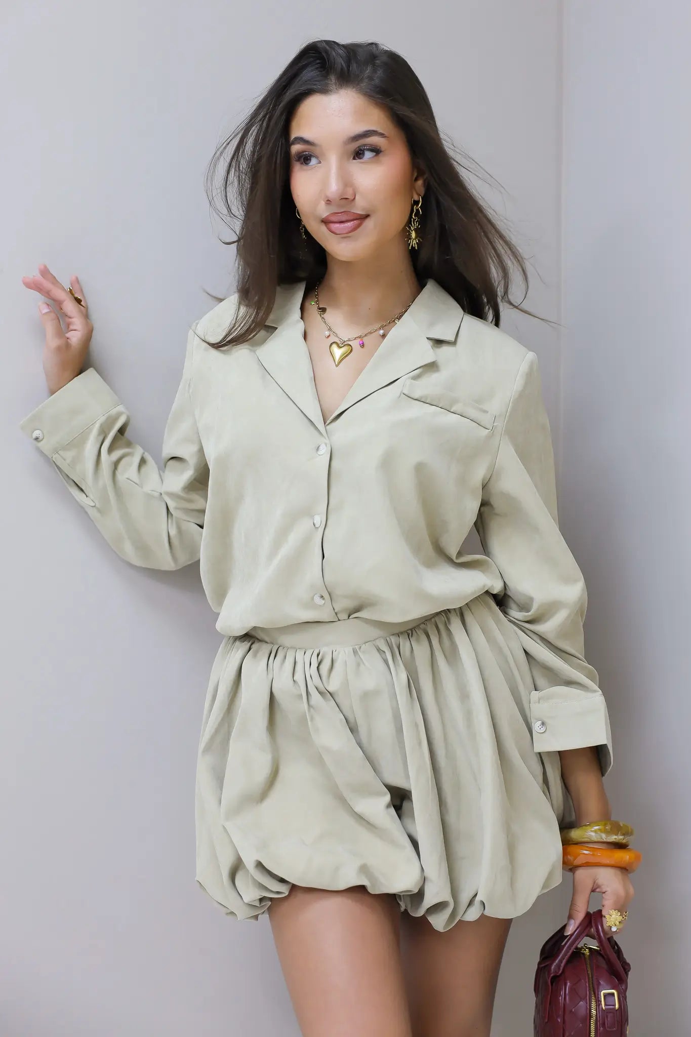 Model draagt beige blouse bij een lichtgrijze muur