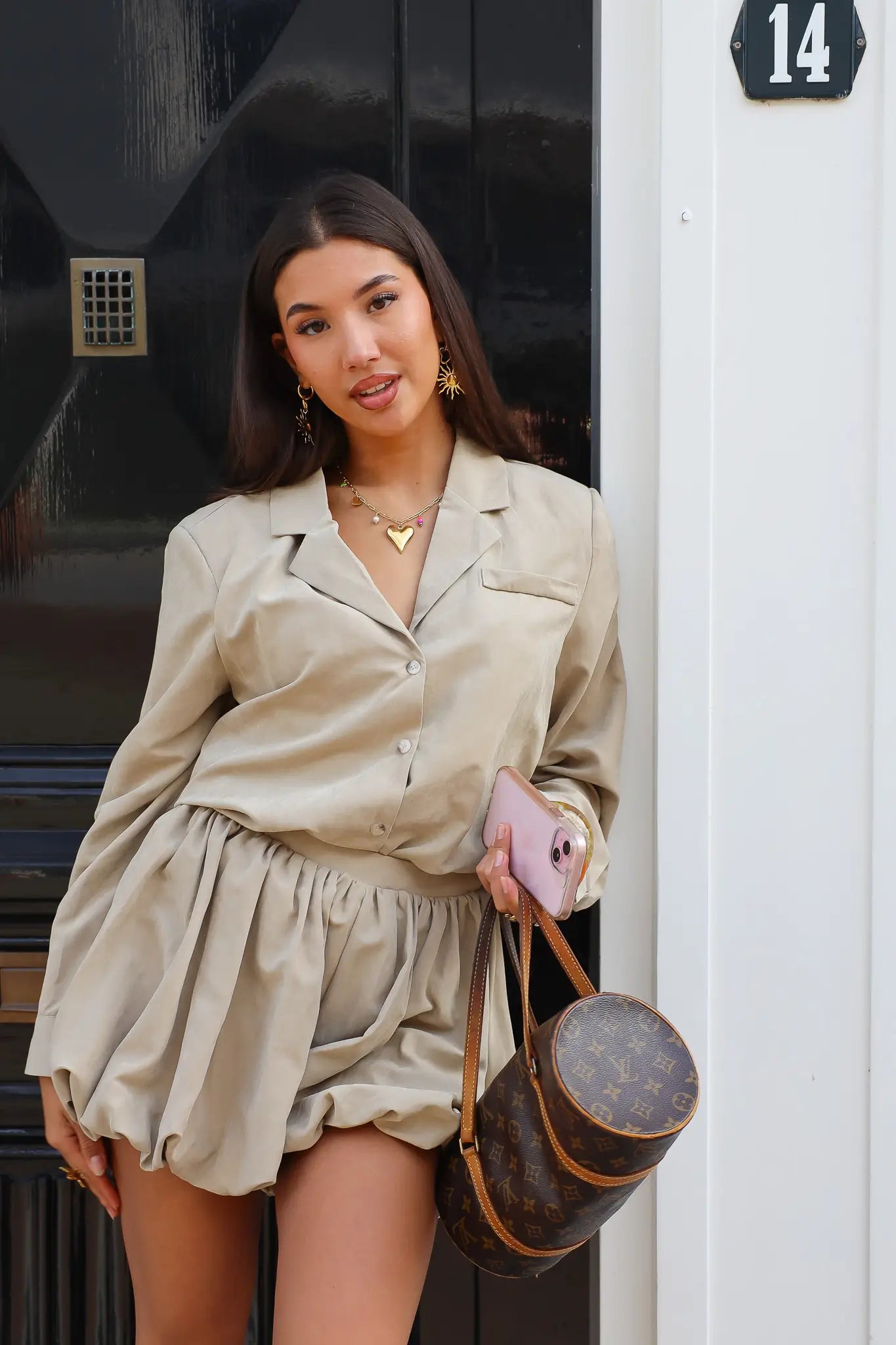 Vrouw draagt beige blouse met kraag buiten voor een zwarte deur