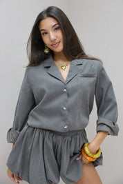 model draagt grijze blouse staand bij muur