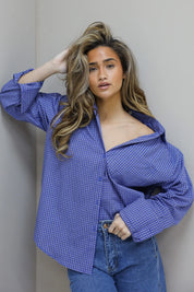 model draagt blauwe blouse met kleine ruit print en schoudervulling