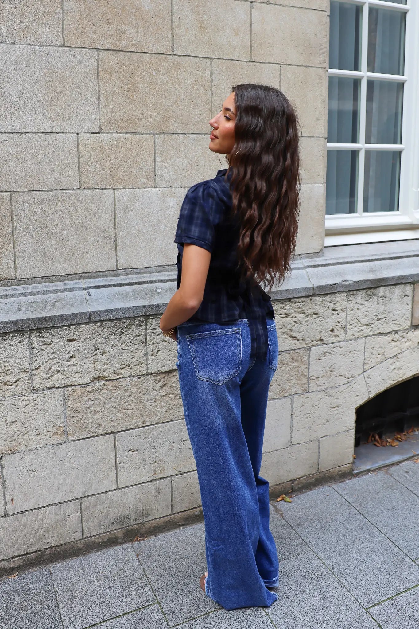 Achteraanzicht van een donkerblauwe geruite blouse met korte mouwen, gedragen bij een blauwe wide leg jeans.