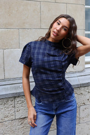 Model draagt een getailleerde donkerblauwe geruite blouse met korte mouwen en knoopdetails bij een blauwe jeans.