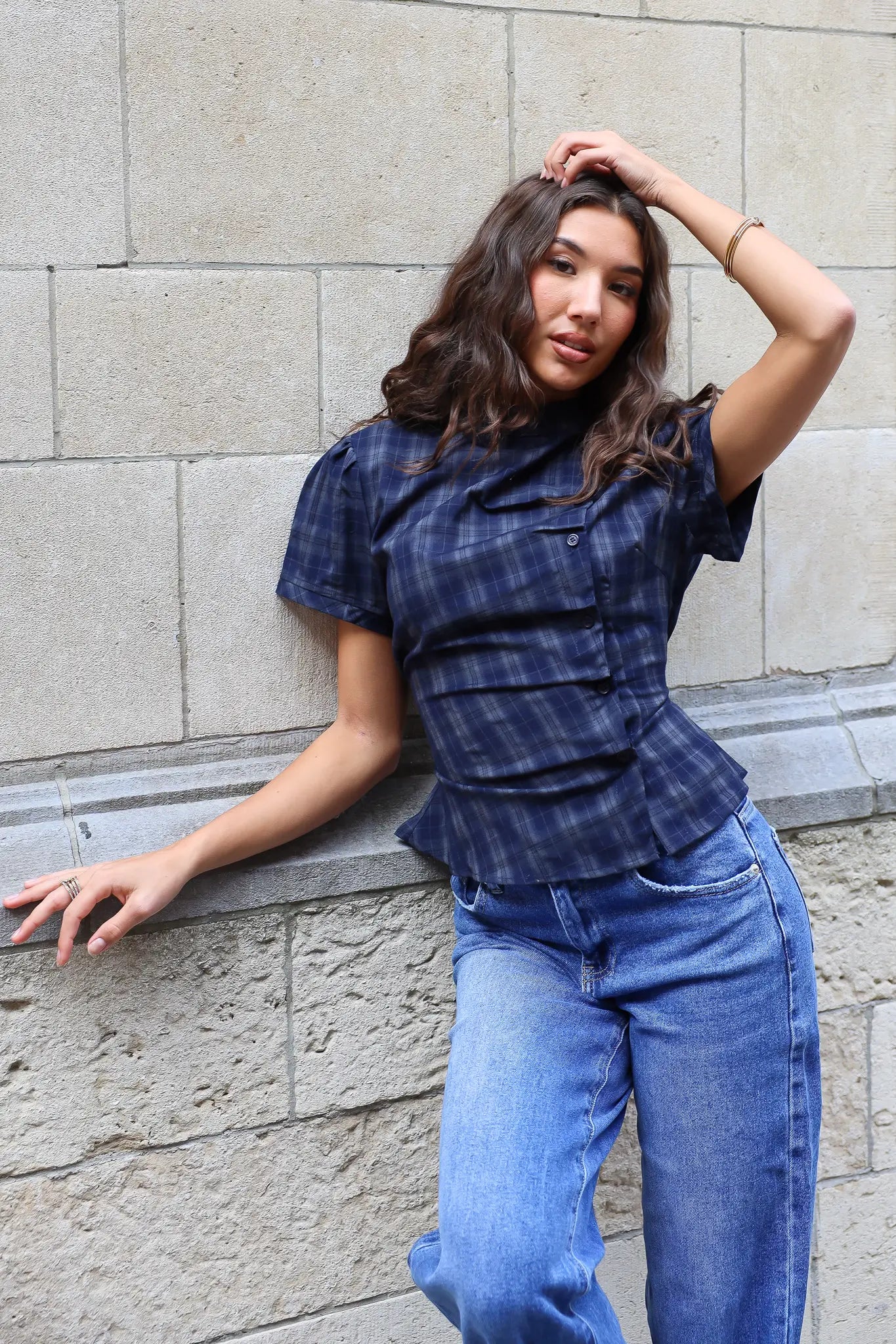 Model draagt een donkerblauwe geruite blouse met korte mouwen, knoopdetails en getailleerde pasvorm, gecombineerd met een lichtblauwe jeans.