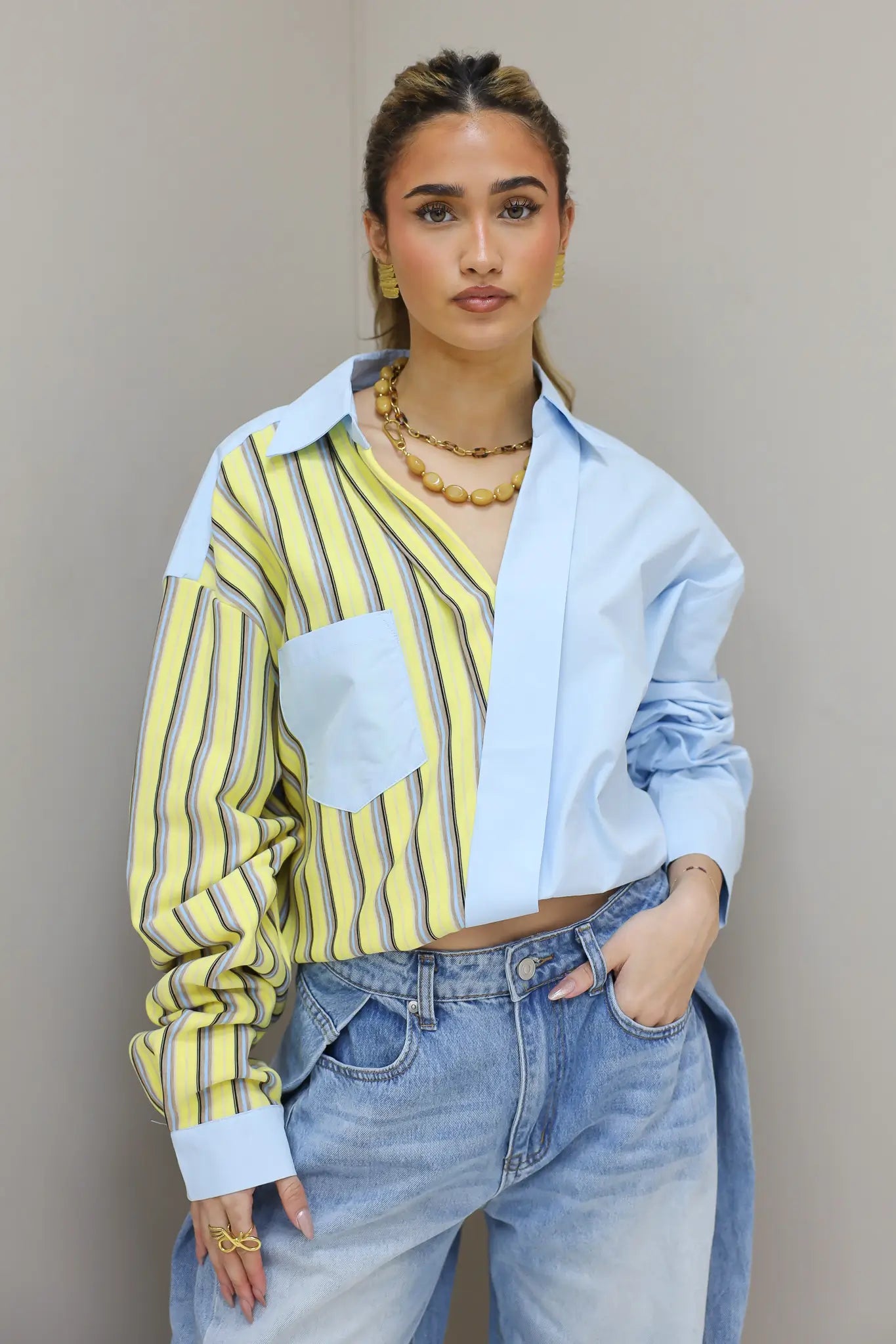 Model draagt asymmetrische blouse met gele strepen en lichtblauw paneel in close up