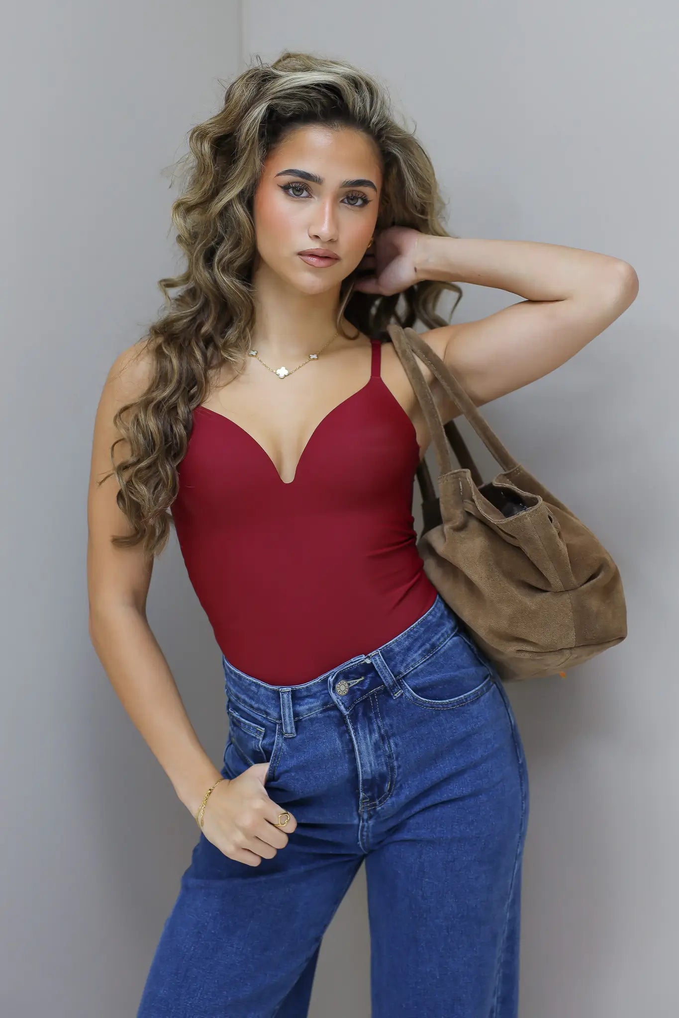 Model draagt bordeaux bodysuit met jeans en bruine tas over schouder