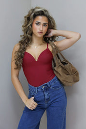 Model draagt bordeaux bodysuit met jeans en bruine tas over schouder