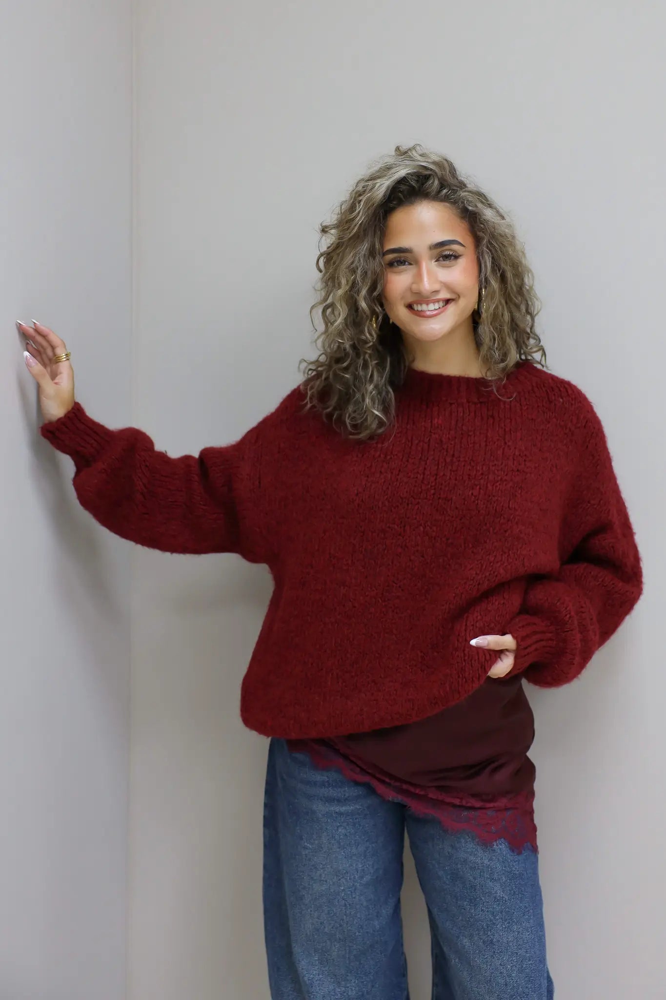 model draagt trui over rode top met kant en denim broek