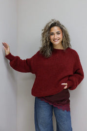 model draagt trui over rode top met kant en denim broek