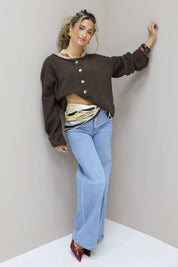 model poseert naast muur in bruin vest en jeans