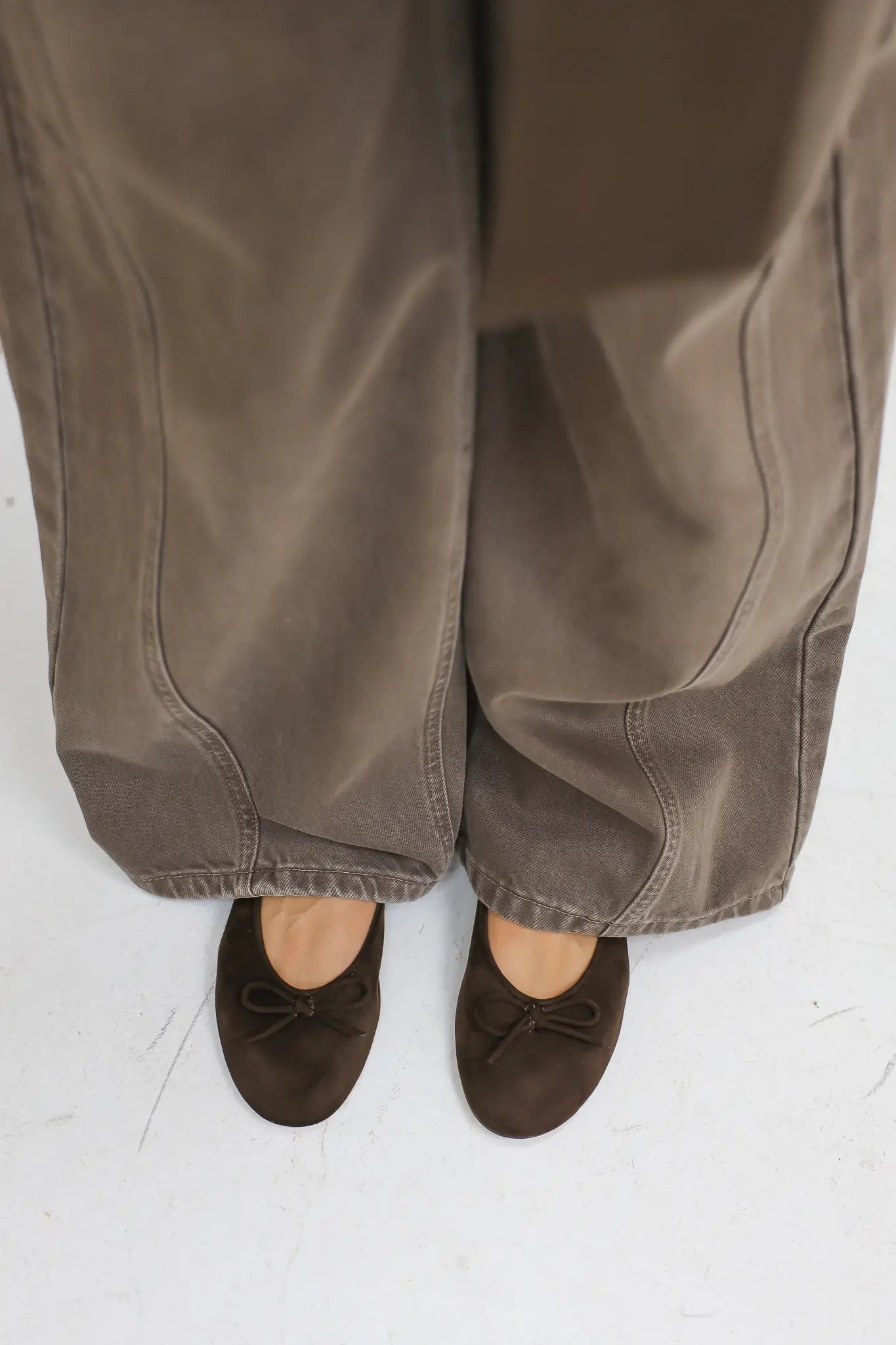 Close up van bruine suède ballerina’s onder een brede broek