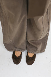 Close up van bruine suède ballerina’s onder een brede broek