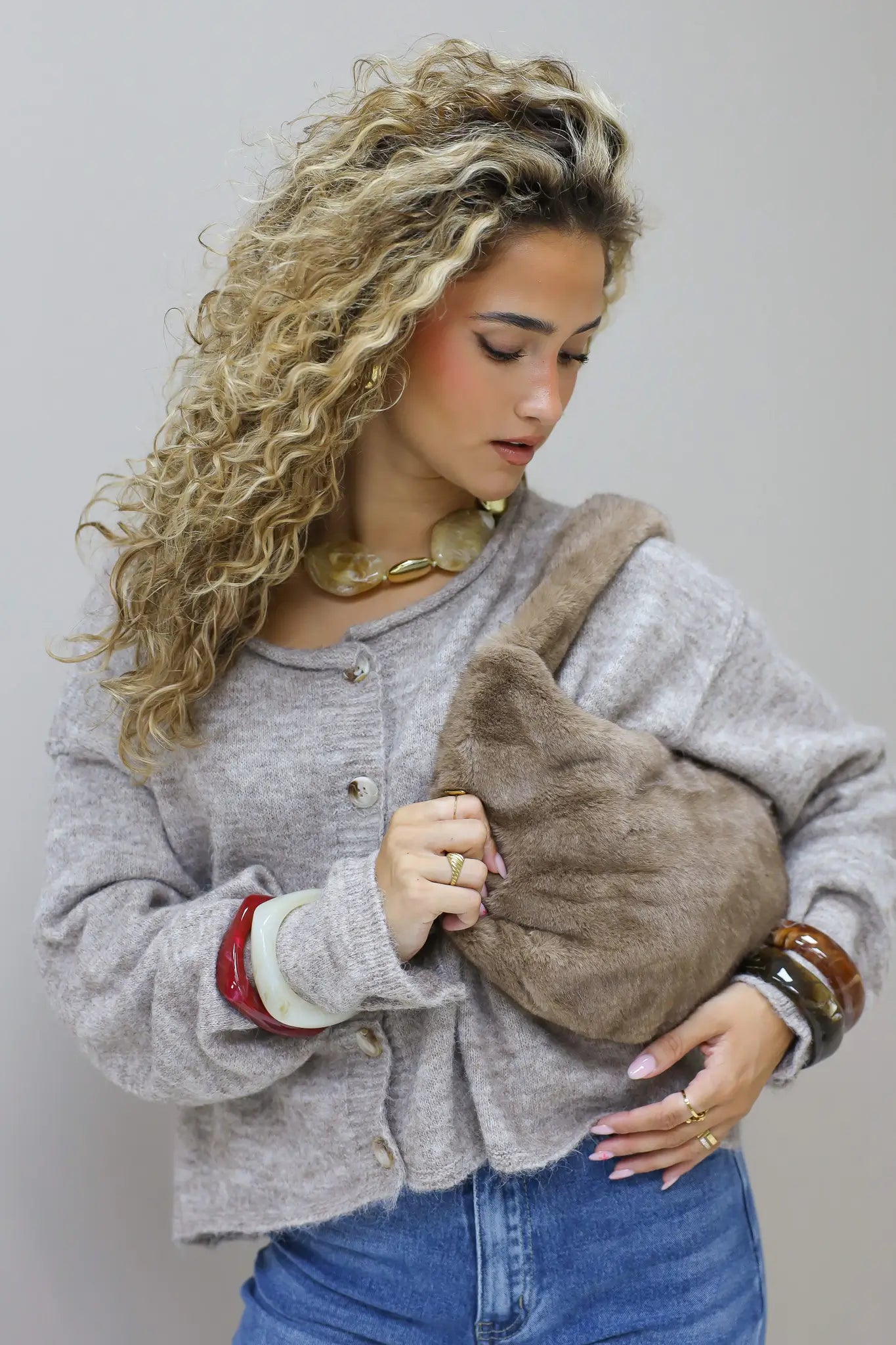 model met krullen houdt een bruine faux fur tas vast voor zich