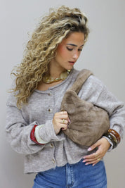 model met krullen houdt een bruine faux fur tas vast voor zich