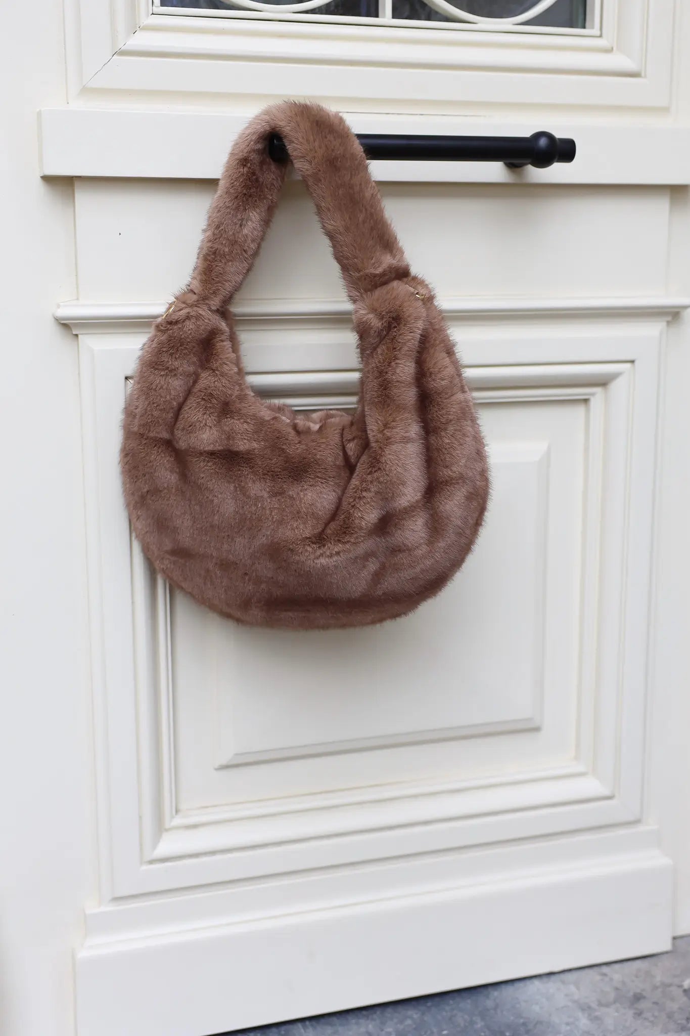 bruine faux fur handtas hangend aan witte deur