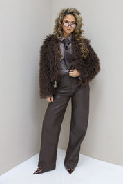 Model met lange haren in bruine fur jas tegen witte muur