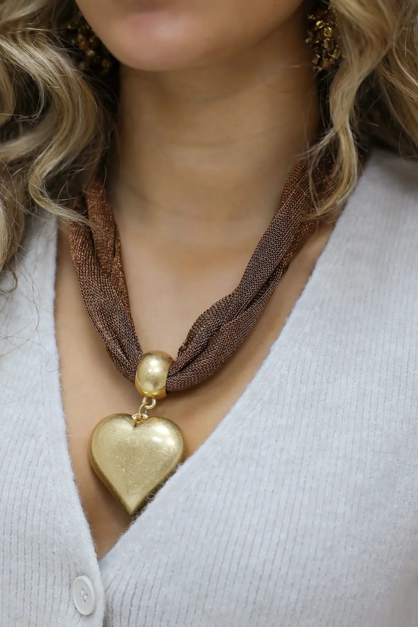 model draagt bruine ketting met goud hart en glimlacht licht richting camera