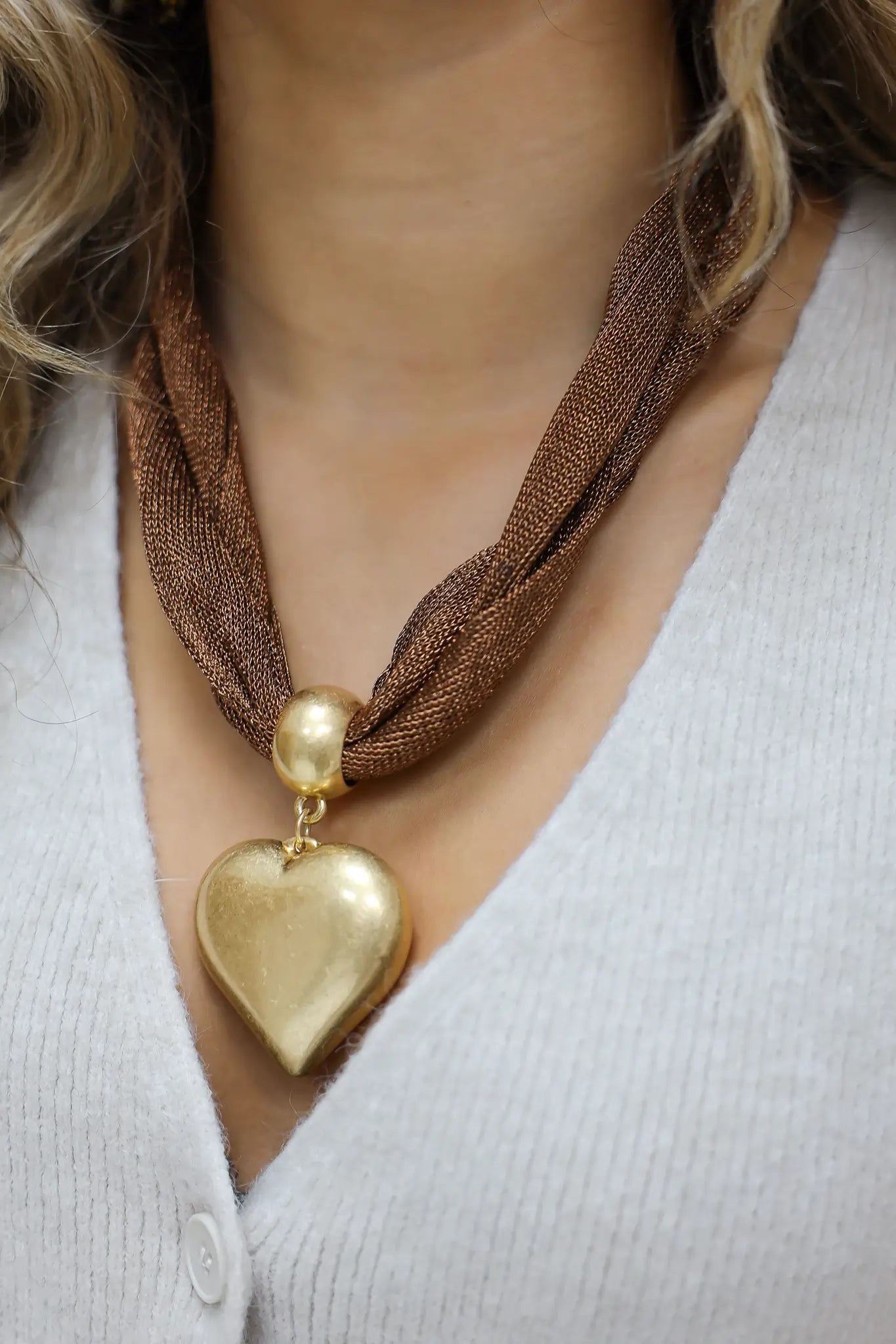 close-up van bruine ketting met groot goudkleurig hart aan hals van model