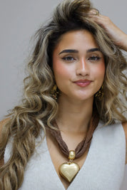 foto van bruine ketting met groot goudkleurig hart aan hals van model